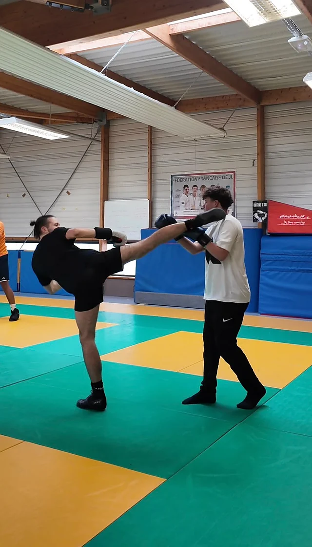 Un boxeur porte un coup de pied haut dans les gants de son partenaire.