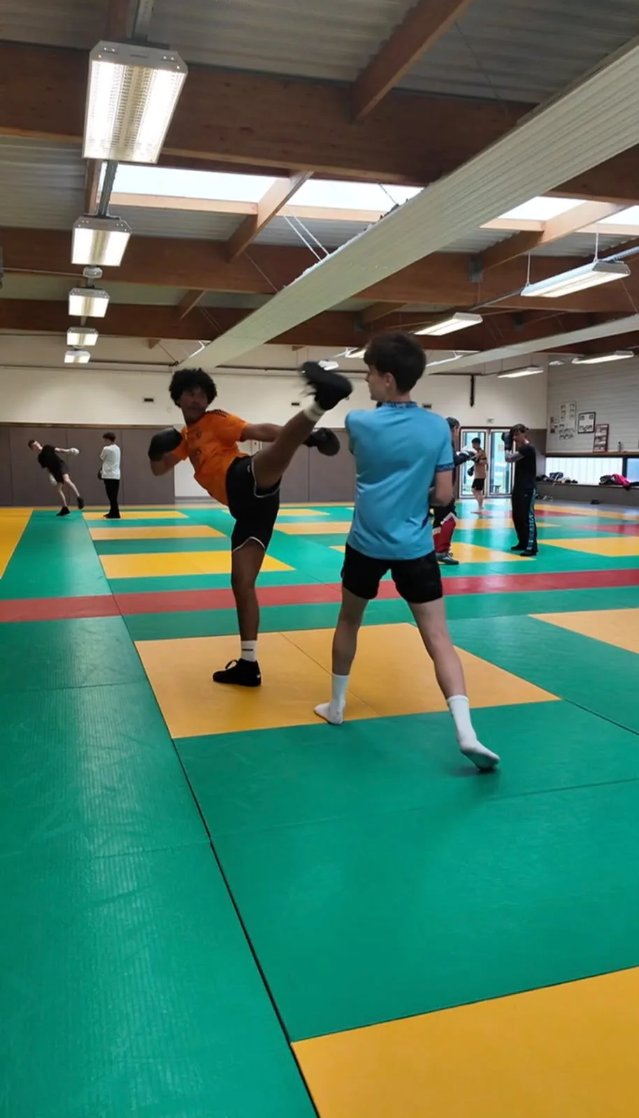 Coup de pied haut d’un boxeur en maillot orange face à son partenaire.
