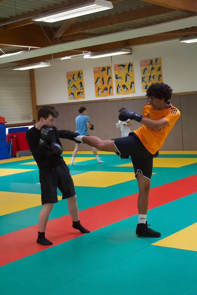 Un boxeur en maillot orange frappe du pied dans une cible tenue par son partenaire.